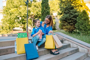 sale, consumerism and people concept - happy young women her dauther with shopping bags walking city street