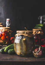 Harvest Preserve Concept. Glass Jar With Fermented Pickled Cucumber On Dark Rustic Kitchen Table With Other Preserve For For The Winter Season. Canning And Conservation Of Harvest. Healthy Food