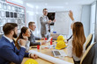 © Dusan Petkovic - Young successful Caucasian architect talking about new project and answering questions. At desk his colleagues sitting and asking more about project.