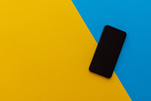 New Modern Black Phone On Yellow And Blue Background, Flat Lay, Copy Space