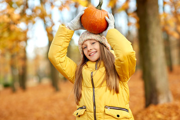 Poster - childhood, season and people concept - happy girl with pumpkin at autumn park