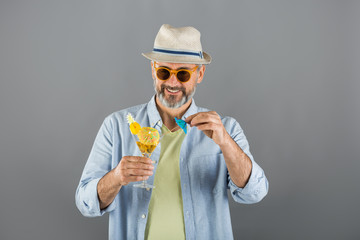 portrait of middle aged man summer dressed drinking cocktail on gray background