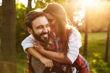 Poster - Image of bearded man giving piggyback ride to pretty woman in green park