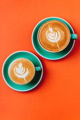 Cyan cappuccino coffee cups over orange background. Top view flat lay with copy space