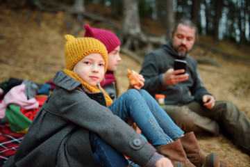 Wall Mural - cute little sisters and their father having picnic by a bonfire on cold autumn day. children having 
