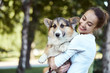 © vitaliymateha - Portrait of a smiling young woman holding cute dog Welsh Corgi in a park outdoors. Beautiful happy female in white shirt playing with her Welsh Corgi Pembroke doggy outside. Concept friendship with