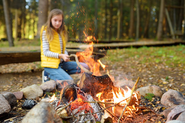 Wall Mural - adorable young girl roasting marshmallows on stick at bonfire. child having fun at camp fire. campin
