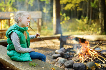 Wall Mural - adorable young girl roasting marshmallows on stick at bonfire. child having fun at camp fire. campin