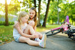 © MNStudio - Adorable girl comforting her little sister after she fell off her bike at summer park. Child getting hurt while riding a bicycle.