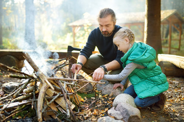 Wall Mural - cute young girl learning to start a bonfire. father teaching her daughter to make a fire. child havi