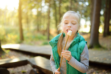 Wall Mural - Adorable young girl roasting marshmallows on stick at bonfire. Child having fun at camp fire. Camping with children in fall forest.