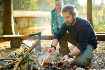 Wall Mural - cute young girl learning to start a bonfire. father teaching her daughter to make a fire. child havi