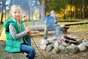 Wall Mural - cute little sisters and their father roasting marshmallows on sticks at bonfire. children having fun