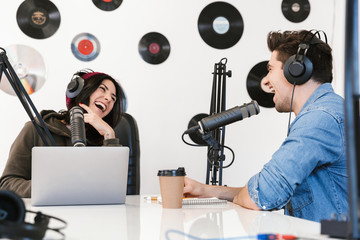 Wall Mural - Young man radio host with colleague woman at the workspace with microphone and sound equipment talking with each other.