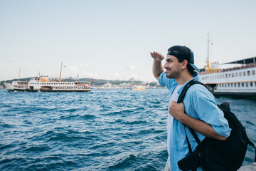 Portrait of a young man against the background of the sea, city, pier and ships.