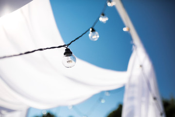 One long electric garland for lighting with white light bulbs against the background of a blue clear sky. Bokeh..Decorative wedding arch with bright bulbs