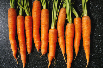 Wall Mural - Young carrot with tops in row over black texture background. Flat lay, space. Cooking concept, food background.