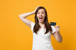 © ViDi Studio - Portrait of surprised young woman in casual clothes keeping mouth open, putting hand on head, hold credit bank card isolated on yellow orange background. People lifestyle concept. Mock up copy space.