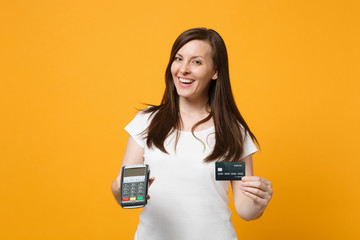 Cheerful young woman holding wireless modern bank payment terminal to process and acquire credit card payments isolated on yellow orange wall background. People lifestyle concept. Mock up copy space.