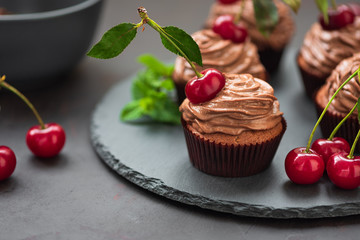 Wall Mural - Chocolate cupcakes with ripe red cherries on dark wooden background. Selective focus. Unhealthy food