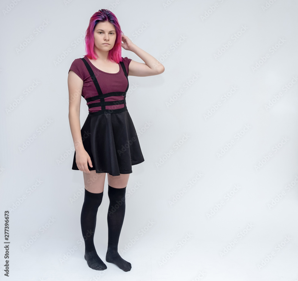 Full-length portrait of young pretty teenager girl in burgundy T-shirt and black dress with beautiful purple hair on a white background in the studio. Talking, smiling, showing hands with emotions.