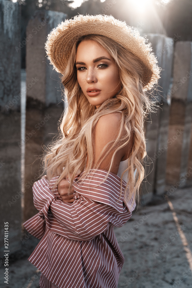 Sensual, attractive and magnificent young woman with long loose blonde hair in a straw hat. Countryside landscape, sunshine at the background. Summertime, summer outdoor lifestyle photoshoot
