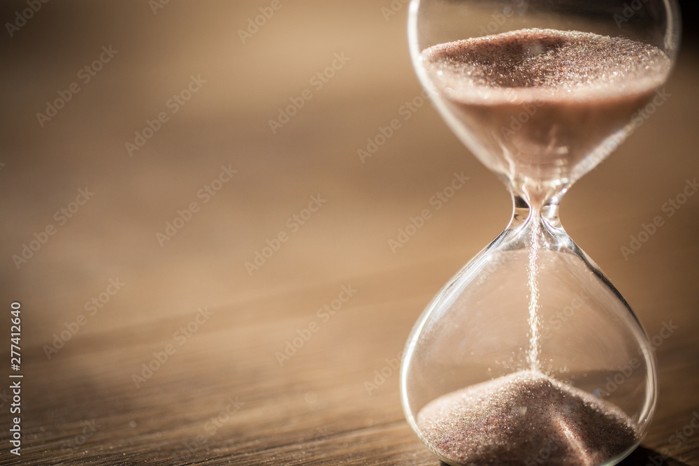 Sand running through the bulbs of an hourglass measuring the passing time in a countdown to a deadline with copy space. - obrazy, fototapety, plakaty 