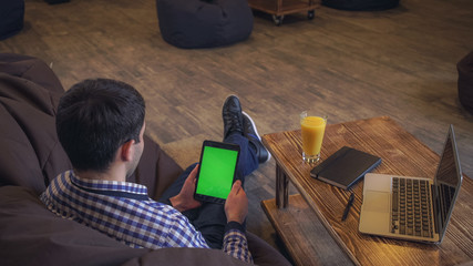 Poster - The man sits back in the hands holding the tablet, welcome companion, a green screen.