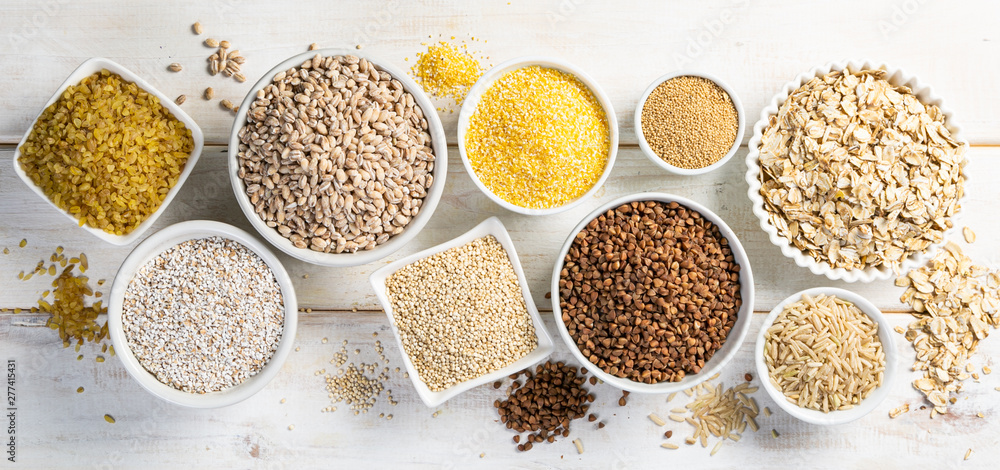 Selection of whole grains in white bowls - rice, oats, buckwheat, bulgur, porridge, barley, quinoa, amaranth, on white wood background - obrazy, fototapety, plakaty 