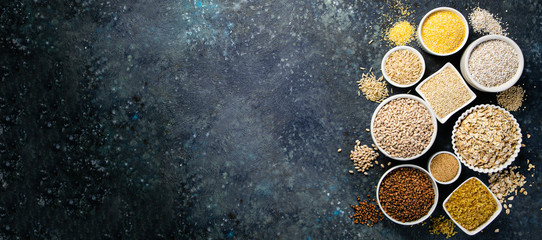 Selection of whole grains in white bowls - rice, oats, buckwheat, bulgur, porridge, barley, quinoa, amaranth on dark background