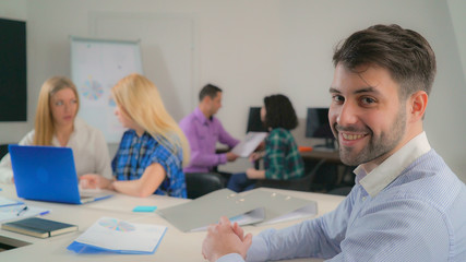 Poster - Portrait handsome mixed race man in office startup company. Young businessman looking at the camera with friendly smile. Professional male with beard smiling. On the background working business team.