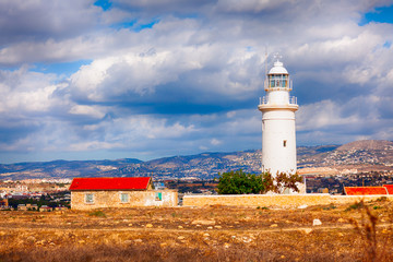 White lighthouse in Paphos Archaeological Park Cyprus and old house.