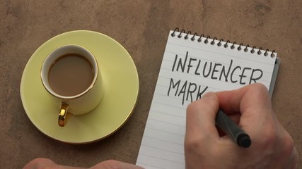 Canvas Print - influencer marketing - a man hand writing a note with a black marker in a notebook, overhead view wi