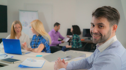 Poster - Portrait handsome mixed race man in office startup company. Young businessman looking at the camera with friendly smile. Professional male with beard smiling. On the background working business team.