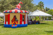 Vintage Colorful Small Gazebo Bounce House Inflated Next To A Tent Selling Souvenirs For All Who Visit The Festival. The Sunny Open Tropical Field Is The Perfect Spot For Community People To Enjoy .