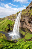 Fototapeta Mapy - Charming beautiful waterfall Seljalandsfoss in Iceland with rainbow. Exotic countries. Amazing places. Popular tourist atraction.