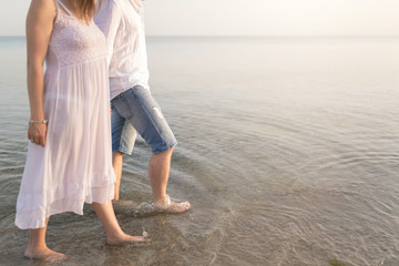 Outdoor shot of romantic young couple walking along the sea shore holding hands. Young man and woman walking on the beach together at sunset, body closeup