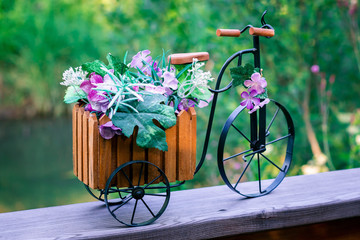 Decorative small wooden bicycle with metal wheels with artificial flowers on the background of nature