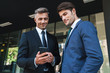© Drobot Dean - Portrait of professional businessmen partners standing outside job center and using cellphone together during working meeting
