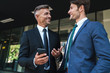 © Drobot Dean - Portrait of happy businessmen partners standing outside job center and using cellphone together during working meeting