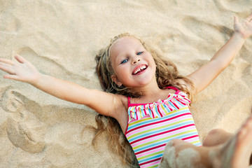 Top view of happy little blonde girl enjoy holiday lying on sandy beach