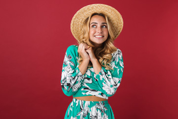 Wall Mural - Excited young beautiful blonde cute woman in dress posing isolated over red wall background looking aside.