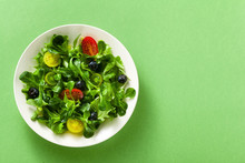 Fresh Salad Of Arugula And Valerian Leaves With Colored Tomatoes And Blueberries In A Plate On A Green Background.
