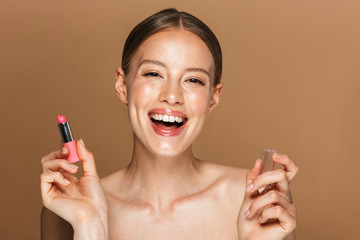 Image closeup of positive half-naked woman smiling at camera and applying lipstick