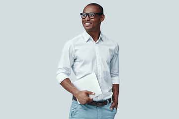 Smart and young. Handsome young African man using digital tablet and smiling while standing against grey background