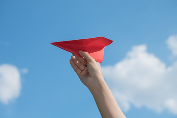 Woman hand holding a red paper rocket with a bright blue background.