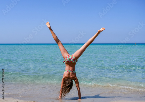 Fotomural Slim and athletic girl doing a handstand before a wonderful beach with crystal c