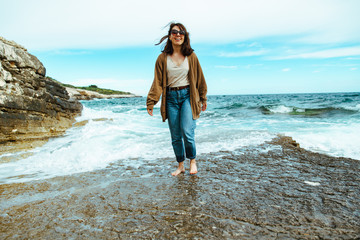 Wall Mural - woman walking by rocky sea beach at sunny windy day. summer vacation