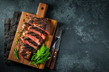Sliced Steak Ribeye, Grilled With Pepper, Garlic, Salt And Thyme Served On A Wooden Cutting Board On A Dark Stone Background. Top View With Copy Space. Flat Lay