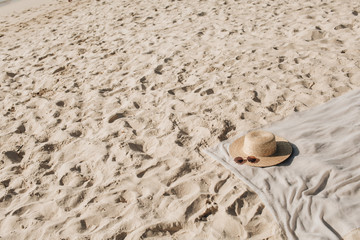 Tropical beautiful beach with white sand, foot steps, neutral blanket with straw hat and sunglasses. Relaxing atmosphere. Summer travel or vacation concept. Minimalistic background.